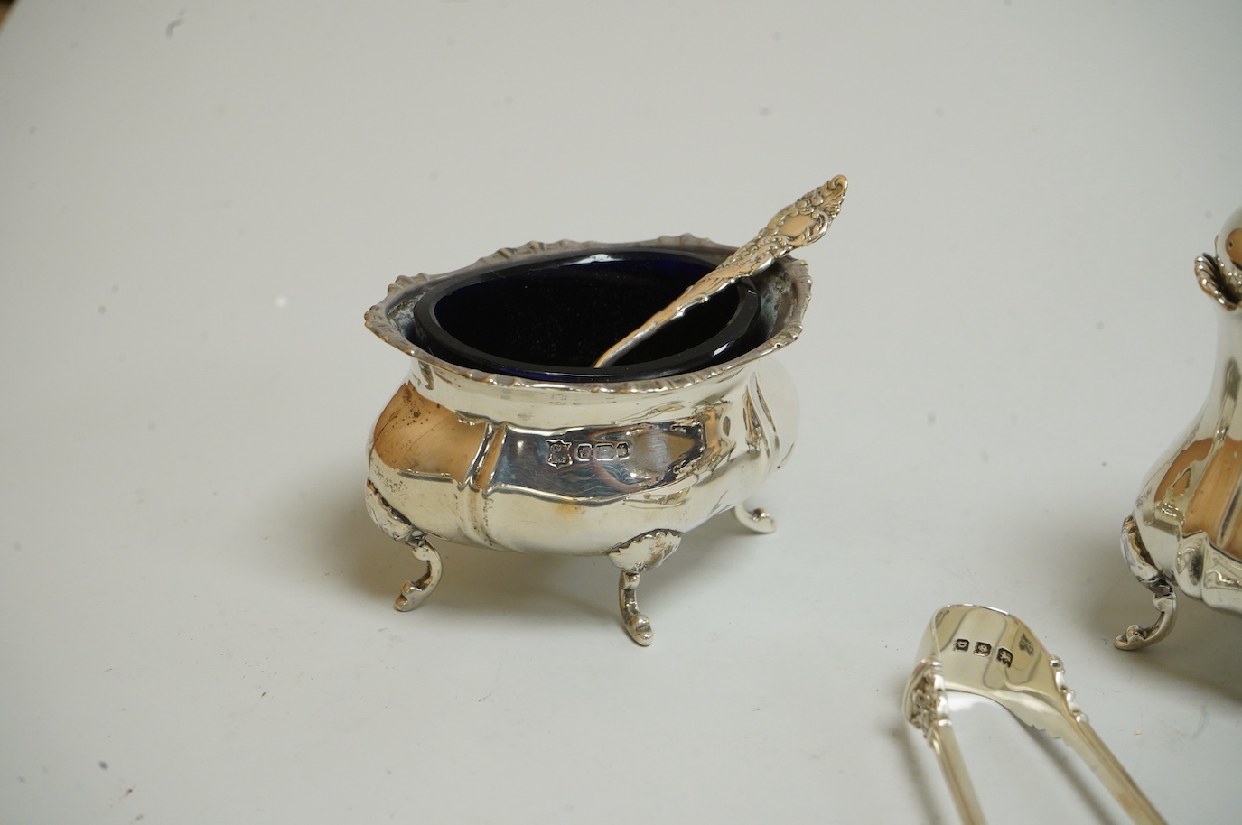 A George V silver sauceboat by Mappin & Webb, Birmingham, 1933, length 16.2cm, together with a silver salt and spoon, with blue glass liner, a silver pepperette, a pair of silver sugar tongs and a Spanish white metal two